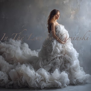 Puede incluir: Una mujer con un vestido de maternidad blanco roto y fluido con una falda y un corpiño voluminosos. El vestido presenta capas de tela suave, creando un efecto de nube. El fondo es gris apagado con el texto "In The Lens by Kaminski".