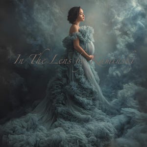 May include: A woman in a flowing, off-the-shoulder gown poses in a dreamy, cloud-filled setting. The dress is a soft, muted blue-green with layers of ruffles. The image has the text "In The Lens by Kaminski" in the lower left corner.