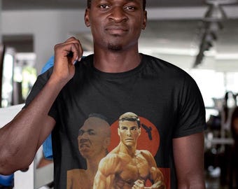 Könnte beinhalten: Ein schwarzes T-Shirt mit einem Vintage-Grafikdruck eines muskulösen Mannes mit dem Text "Kickboxer" auf der Vorderseite.