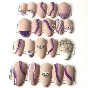 May include: Set of 10 false nails with a nude base and purple swirl design. Some nails have rhinestones.