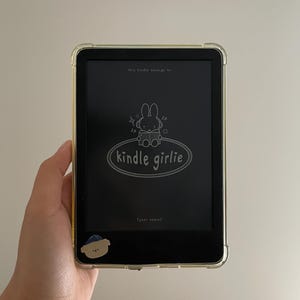 May include: A black and white illustration of a bunny reading a book on a Kindle e-reader. The text on the screen reads "this kindle belongs to... kindle girlie (your name)"