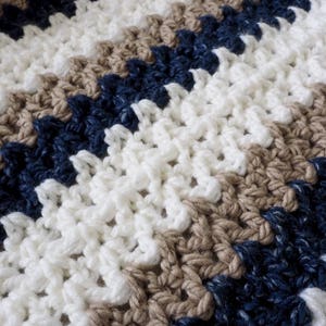 May include: A crocheted blanket with stripes of white, brown, and navy blue yarn.