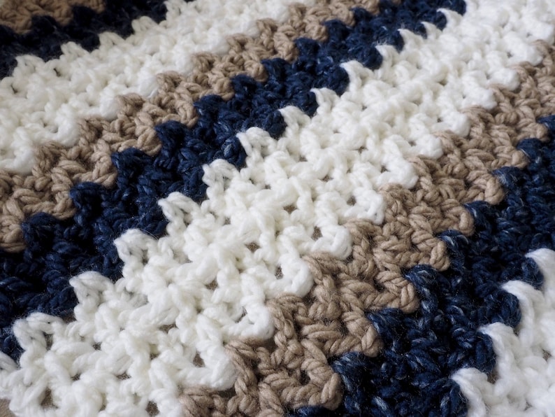 May include: A crocheted blanket with stripes of white, brown, and navy blue yarn.