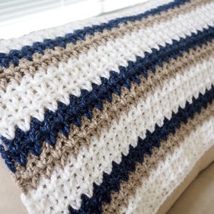 May include: A striped crocheted throw blanket in white, beige, and navy blue.