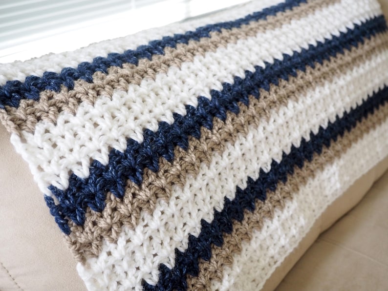 May include: A striped crocheted throw blanket in white, beige, and navy blue.