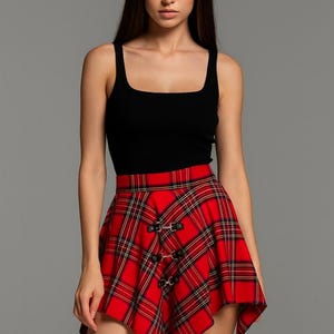 Op de afbeelding: Een zwarte tanktop gecombineerd met een rode geruite rok. De rok heeft een klassiek tartanpatroon met zwarte accenten en decoratieve gespen. De outfit is een stijlvolle combinatie van casual en edgy elementen.
