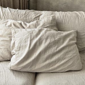 Peut inclure: Gros plan d'un lit avec deux oreillers en lin beige et une housse de couette assortie. Les oreillers sont rectangulaires et légèrement froissés, suggérant le confort. La palette de couleurs neutres crée une atmosphère apaisante, idéale pour une chambre.