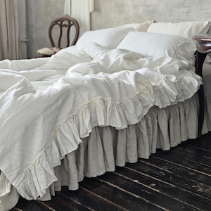 May include: White linen bed skirt with a ruffled edge. The bed skirt is made of a soft, natural fabric and has a simple, elegant design.