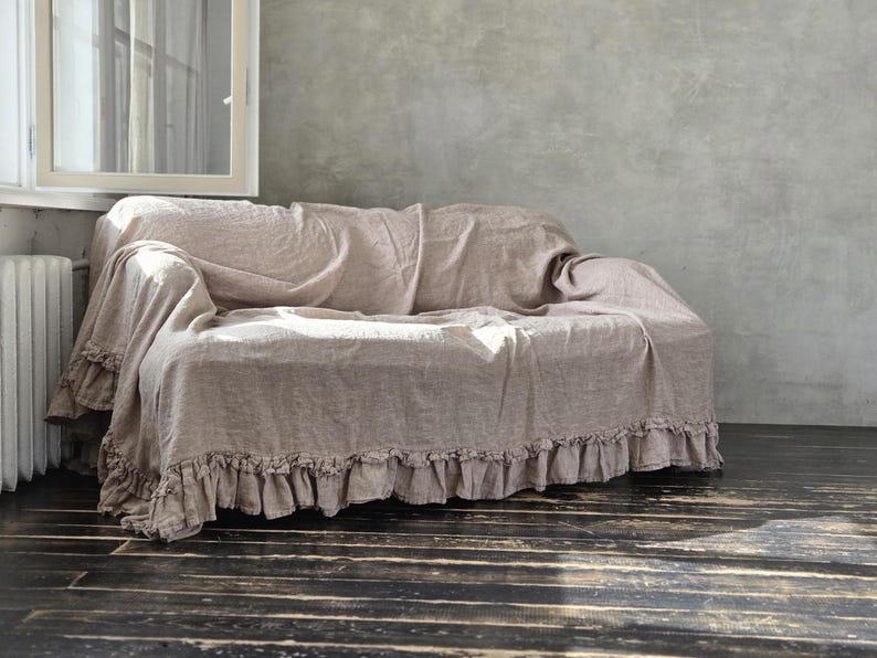 Peut inclure: Une housse de canap&eacute; en lin beige avec une finition en tissu textur&eacute; et un bord &agrave; volants d&eacute;coratif le long de la base. La housse recouvre le dossier, l'assise et les accoudoirs du canap&eacute;, offrant un aspect couvrant avec des plis souples.