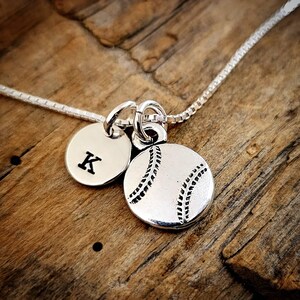 May include: Silver necklace with a baseball charm and a charm with the letter K.