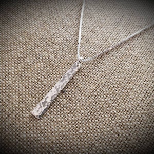 May include: A silver necklace with a hammered, rectangular pendant. The pendant is hanging on a silver chain.