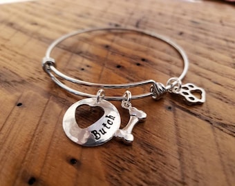 May include: Silver expandable bracelet with a heart charm that says "Butch" and a bone charm. The bracelet also has a paw print charm.