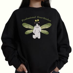 May include: Black sweatshirt with a graphic of a black and white cat with green wings and the text "Professional Overthinker".