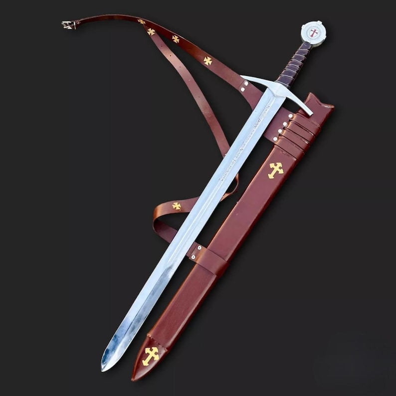 May include: A medieval sword with a silver blade and a brown leather scabbard. The hilt features a white pommel with a red cross. The scabbard and leather strap are adorned with gold crosses. The sword is approximately 40 inches long.