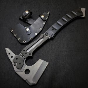 Puede incluir: Un tomahawk t&aacute;ctico con mango negro y hoja plateada, acompa&ntilde;ado de una funda de cuero negro. El tomahawk presenta una hoja afilada, una punta y un dise&ntilde;o de cabeza de martillo. El mango tiene un agarre texturizado.