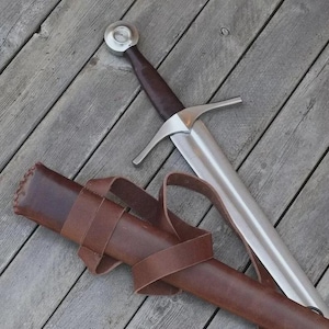 May include: A steel sword with a dark brown leather-wrapped grip, a silver-colored pommel, and a straight crossguard. The sword is accompanied by a matching brown leather scabbard featuring integrated leather straps for carrying or attachment.