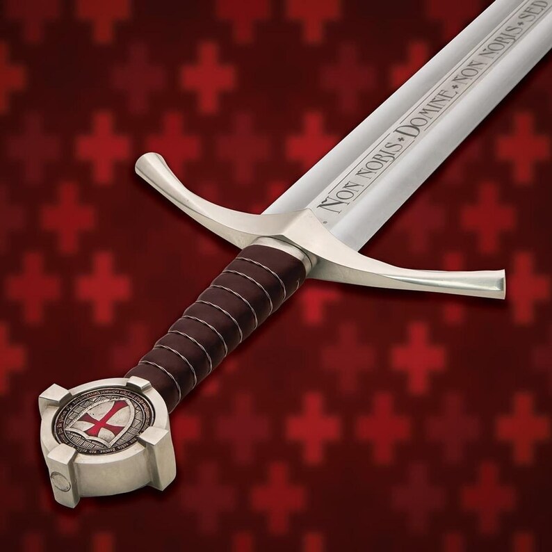 May include: A medieval-style sword with a silver blade and guard, featuring a brown leather-wrapped handle. The pommel displays a red cross emblem. The blade is inscribed with the words "NON NOBIS DOMINE NON NOBIS SED".