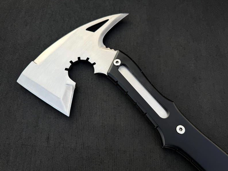 Peut inclure: Une hache tactique argent&eacute;e et noire avec une lame tranchante et un bord dentel&eacute;. La t&ecirc;te de la hache a un design unique avec un dessus incurv&eacute; et une d&eacute;coupe circulaire. Le manche est noir avec un accent blanc.