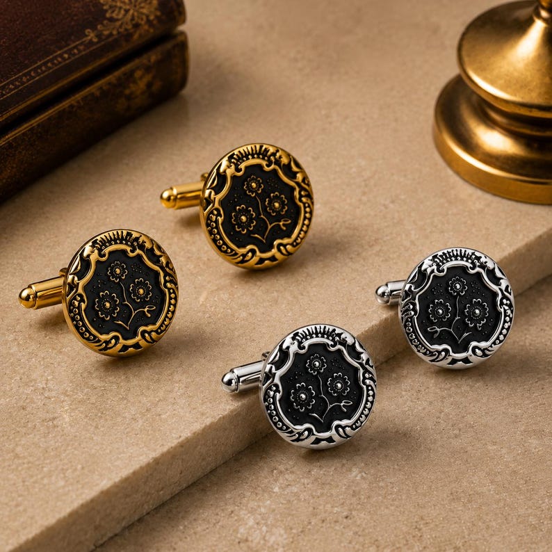 May include: Two pairs of round cufflinks, one pair in gold-tone metal and one pair in silver-tone metal. Each cufflink features a black circular center with an embossed floral design and a decorative border with intricate scrollwork detailing.