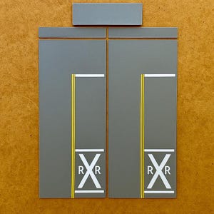 May include: Gray rectangular panels with white and yellow lines and the letters "R" and "X". The panels are arranged to resemble a railroad crossing sign. A smaller gray panel is above the larger panels.