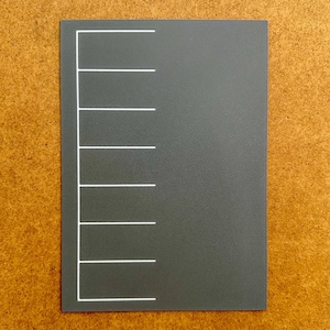 May include: A rectangular, dark gray card with evenly spaced white horizontal lines along the left edge. The card is set against a textured, light brown background.