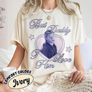 May include: Ivory-colored t-shirt with the text "But Daddy I Love Him" in a cursive font, surrounding a heart-shaped image of a person. The shirt also features the words "Comfort Colors" and "Ivory" in a circular design.
