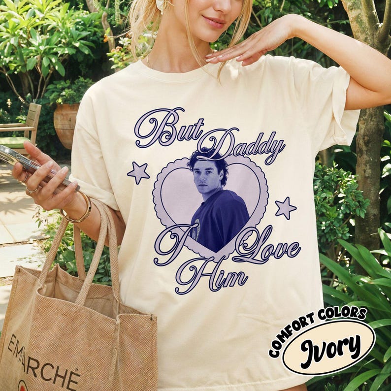 May include: Ivory-colored t-shirt with the text "But Daddy I Love Him" in a cursive font, surrounding a heart-shaped image of a man. The shirt also features star graphics and the words "Comfort Colors Ivory".