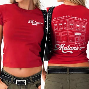 May include: A red short-sleeved t-shirt featuring the white text Malone's on the front. The back displays a white line drawing of a building with the text Best burgers in hastings, ma! and the word Malone's in a large script font below it.