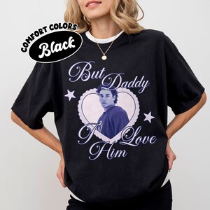 May include: Black comfort colors t-shirt with a heart-shaped graphic featuring a man's image and the text "But Daddy I Love Him". The shirt also has the text "Comfort Colors Black" in a circular design.