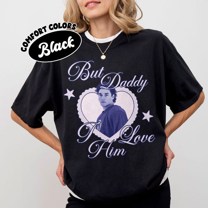 May include: Black comfort colors t-shirt with a heart-shaped graphic featuring a man's image and the text "But Daddy I Love Him". The shirt also has the text "Comfort Colors Black" in a circular design.