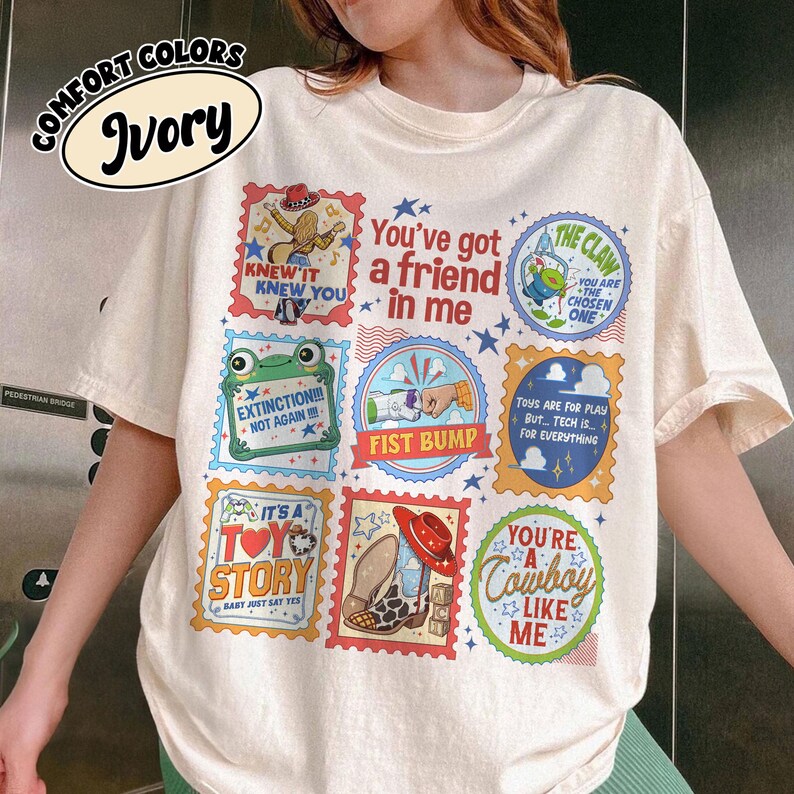 Puede incluir: Una camiseta de color marfil con un estampado gr&aacute;fico multicolor que presenta varias ilustraciones al estilo de sellos postales. El dise&ntilde;o incluye textos como You've got a friend in me, The Claw, Extinction Not Again, Fist Bump y You're a cowboy like me.