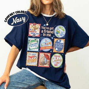 Puede incluir: Una camiseta azul marino con un estampado gr&aacute;fico de varios sellos coloridos cuadrados y circulares. El texto incluye "You've got a friend in me," "Knew it knew you," "Extinction!!! Not again!!!," "Fist bump," "It's a Toy Story," y "You're a cowboy like me."