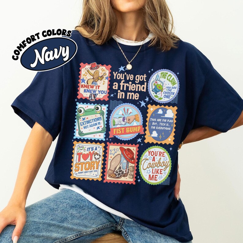 Puede incluir: Una camiseta azul marino con un estampado gr&aacute;fico de varios sellos coloridos cuadrados y circulares. El texto incluye "You've got a friend in me," "Knew it knew you," "Extinction!!! Not again!!!," "Fist bump," "It's a Toy Story," y "You're a cowboy like me."