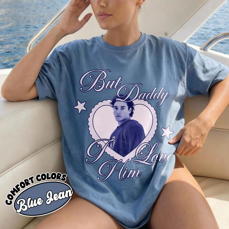 May include: Blue jean colored t-shirt with the text "But Daddy I Love Him" in a cursive font. The shirt features a heart-shaped graphic with a portrait of a man. The words "Comfort Colors" and "Blue Jean" are also visible.
