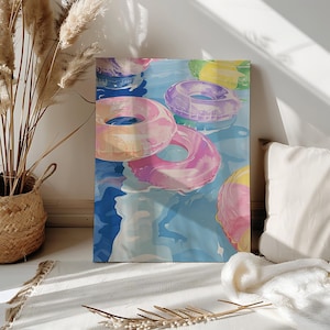 May include: A canvas print depicting a pool scene with colourful inflatable rings. The rings are shades of pink, purple, and yellow, floating on blue water. The artwork evokes a sense of summer and leisure.