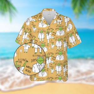 May include: A short-sleeved button-down shirt with a mustard yellow background. The shirt features a repeating pattern of a green frog wearing a white suit, with text that reads "Letting the days go by" and "How did I get here?"