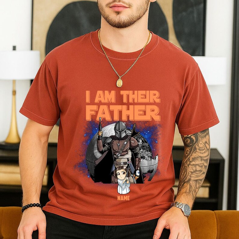 May include: Rust-colored t-shirt with the text "I AM THEIR FATHER" in orange. The graphic features a Mandalorian character and a child, with a space scene backdrop. The word "NAME" is below the child.