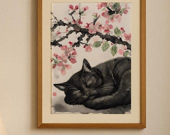 May include: A framed watercolor painting of a sleeping black cat under a flowering tree branch. The artwork is in a wooden frame and hangs above a beige armchair with a cable-knit pillow. A side table with a lamp and vase is in the foreground.