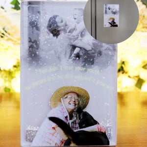 May include: A clear glass block with a glittery background and two photos inside. The top photo shows a woman holding a young child. The bottom photo shows an older woman smiling and holding a dog. The text "You didn't lose your youth" is printed on the glass block.