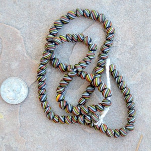 May include: A strand of black, white, orange, and yellow striped glass beads. The beads are round and have a glossy finish.