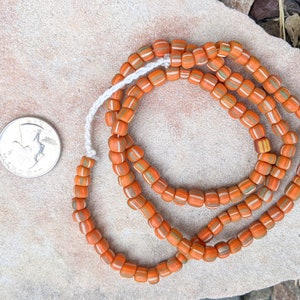 May include: A strand of orange, white and green striped glass beads. The beads are approximately the size of a UK 20 pence coin.