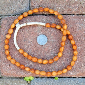 May include: A long strand of brown wooden beads with a white cord woven through the center. The beads are oval shaped and have a natural, rustic look.