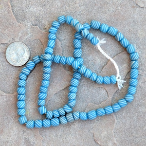 May include: A strand of blue and white striped glass beads. The beads are small and round, and they are strung on a white cord.