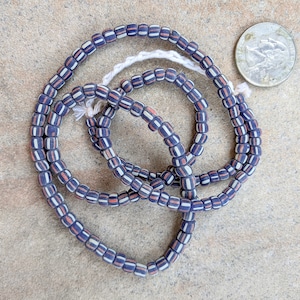 May include: A strand of blue and white patterned glass beads. The beads are small and round, and they are strung together on a thin cord. The beads are arranged in a random pattern, and they are all the same size.
