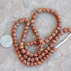 May include: A strand of red, white, and green striped glass beads. The beads are approximately the size of a US quarter.