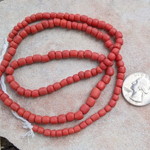 May include: A strand of red glass beads, approximately the size of a US quarter, on a light brown background.