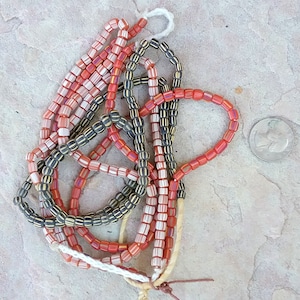 Könnte beinhalten: Eine Sammlung von Vintage-Glasperlen in Rot, Weiß und Schwarz. Die Perlen sind auf einer Schnur aufgefädelt und liegen lose in einem Haufen.