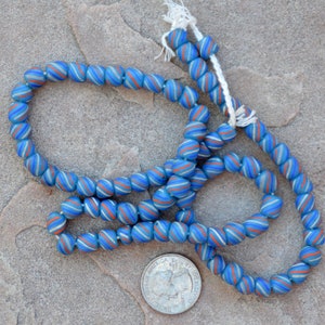 May include: A strand of blue and white glass beads with a red stripe. The beads are round and have a swirl pattern. The beads are strung on a white cord.