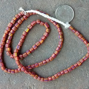 May include: A strand of red, yellow, and blue glass beads. The beads are square shaped and have a white stripe running down the center. The beads are strung on a white cord.