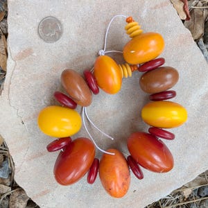 以下が含まれることがあります： オレンジ、イエロー、ブラウンの大きな丸いビーズで作られたネックレス。ビーズは白い紐に通されています。